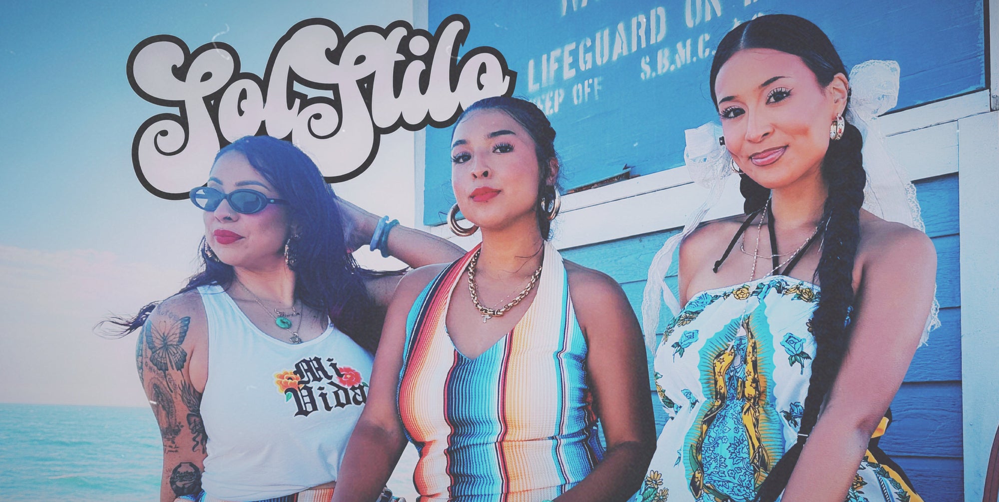 Three women posing together in front of a blue building with the text 'SolStilo' and 'Lifeguard Un.